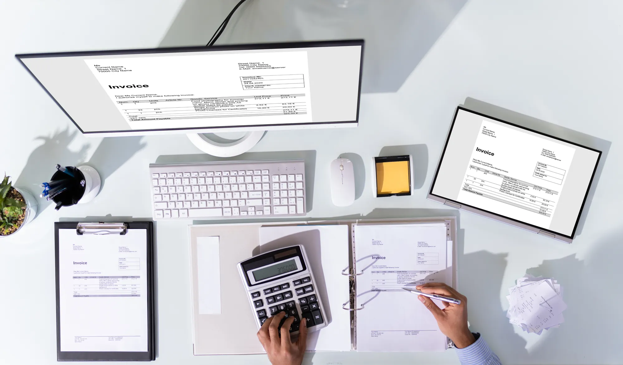 An accountant’s workspace with a computer, tablet, calculator, and printed invoices. A professional is reviewing and calculating the same invoice displayed on the monitor, tablet, and printed document.