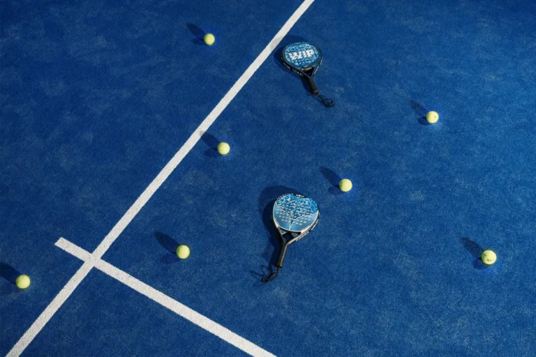 Raket dan bola padel di lapangan biru.
